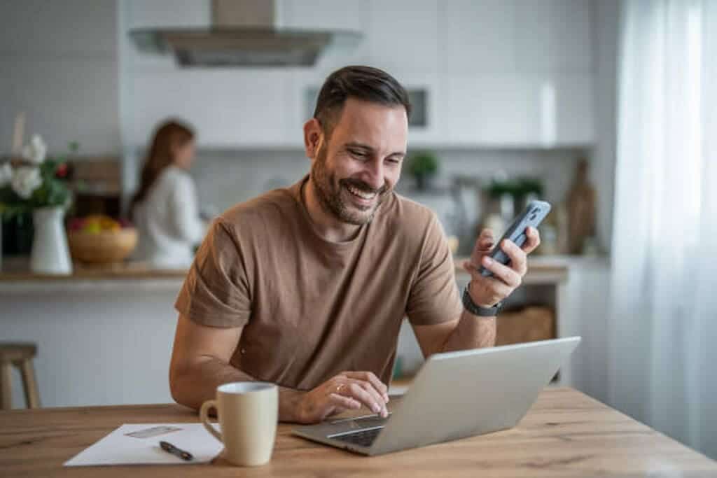 Joven ocupado administrando tareas en su computadora portátil y teléfono