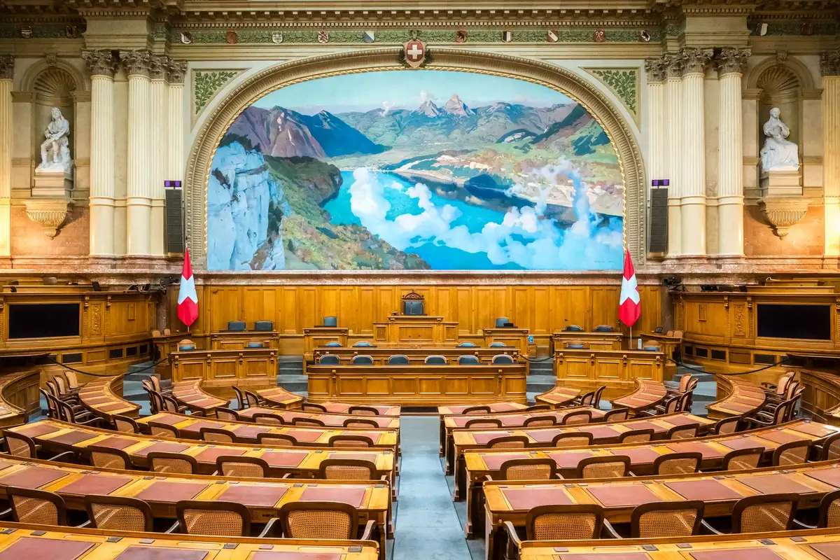 Câmara parlamentar com documentos e assentos legislativos durante debate sobre aquisição de defesa