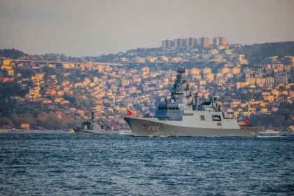Fragata militar atracada numa base naval com estruturas portuárias ao fundo