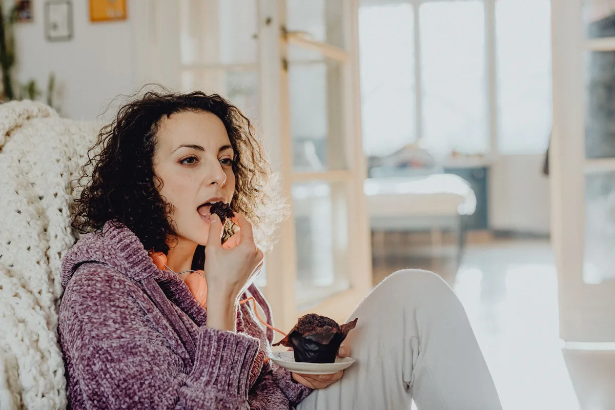 Mãos anónimas a alcançar comida de conforto numa mesa, ilustrando impulso emocional