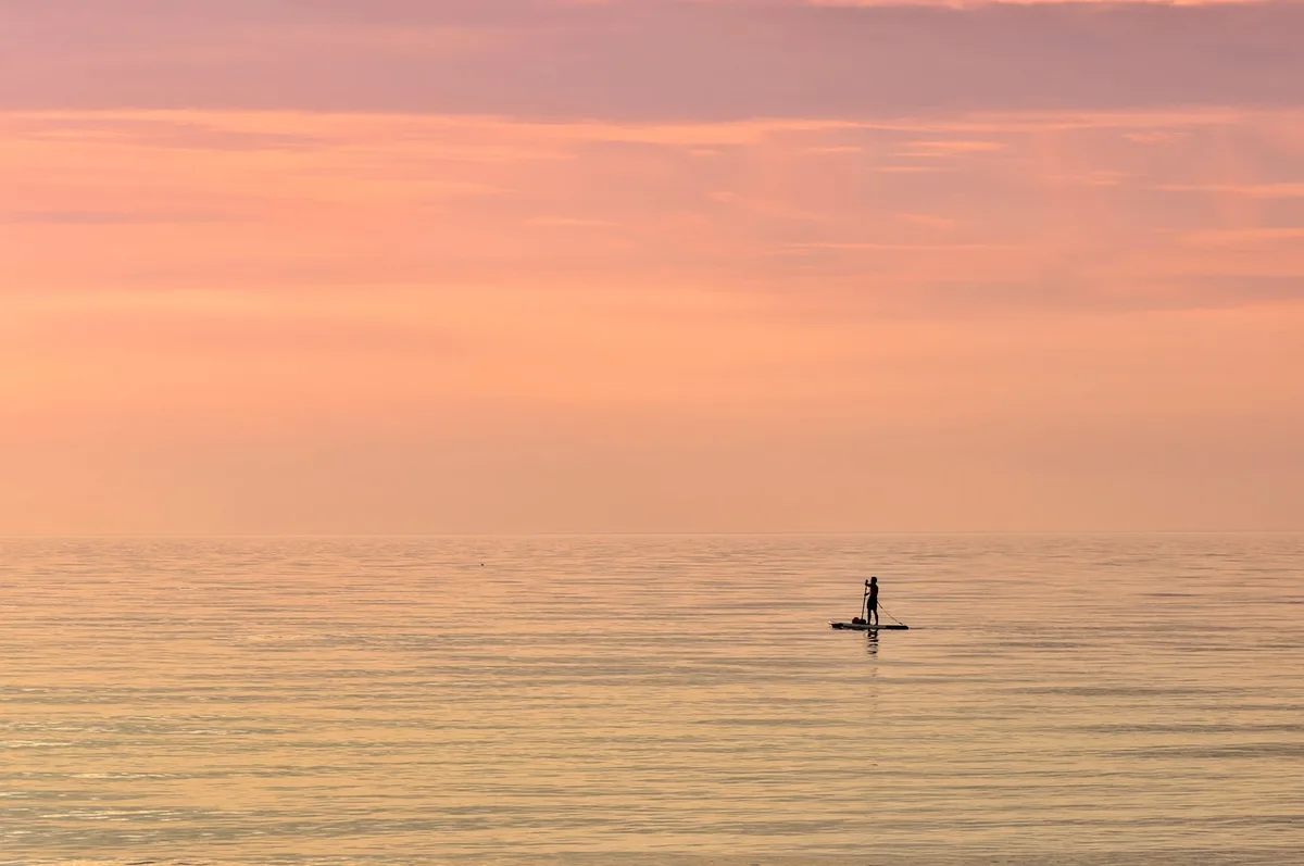 Dois praticantes de stand-up paddle a navegar afastados da costa durante travessia