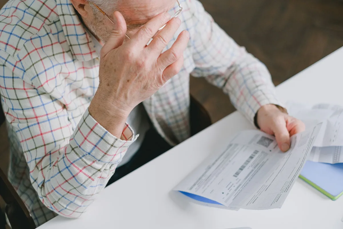 Mãos de um pensionista segurando documentos de pensão e papéis financeiros