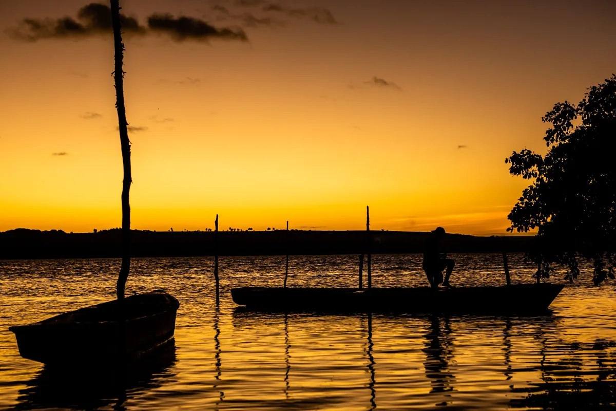 Pessoas em canoagem e stand up paddle no rio ao pôr do sol, com aldeia ao fundo
