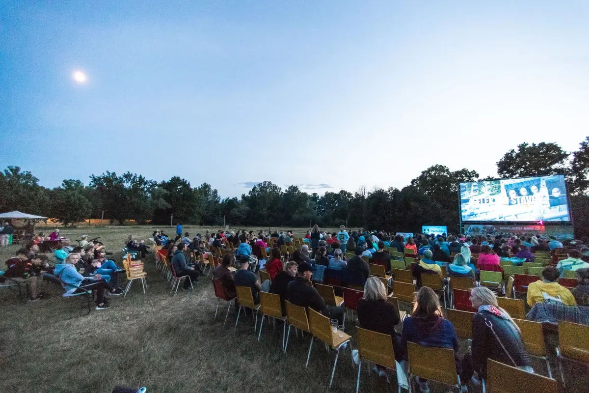 Famílias e casais sentados ao ar livre a assistir a filme numa tela grande iluminada à noite