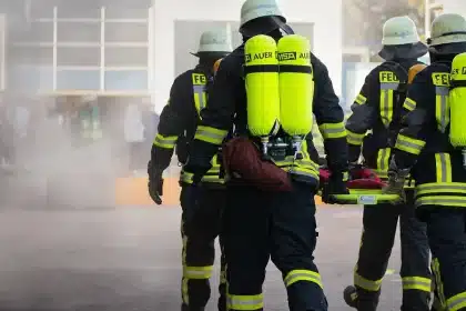 Cidade envolvida em fumo denso com helicópteros de combate a incêndios sobrevoando e veículos de emergência nas ruas