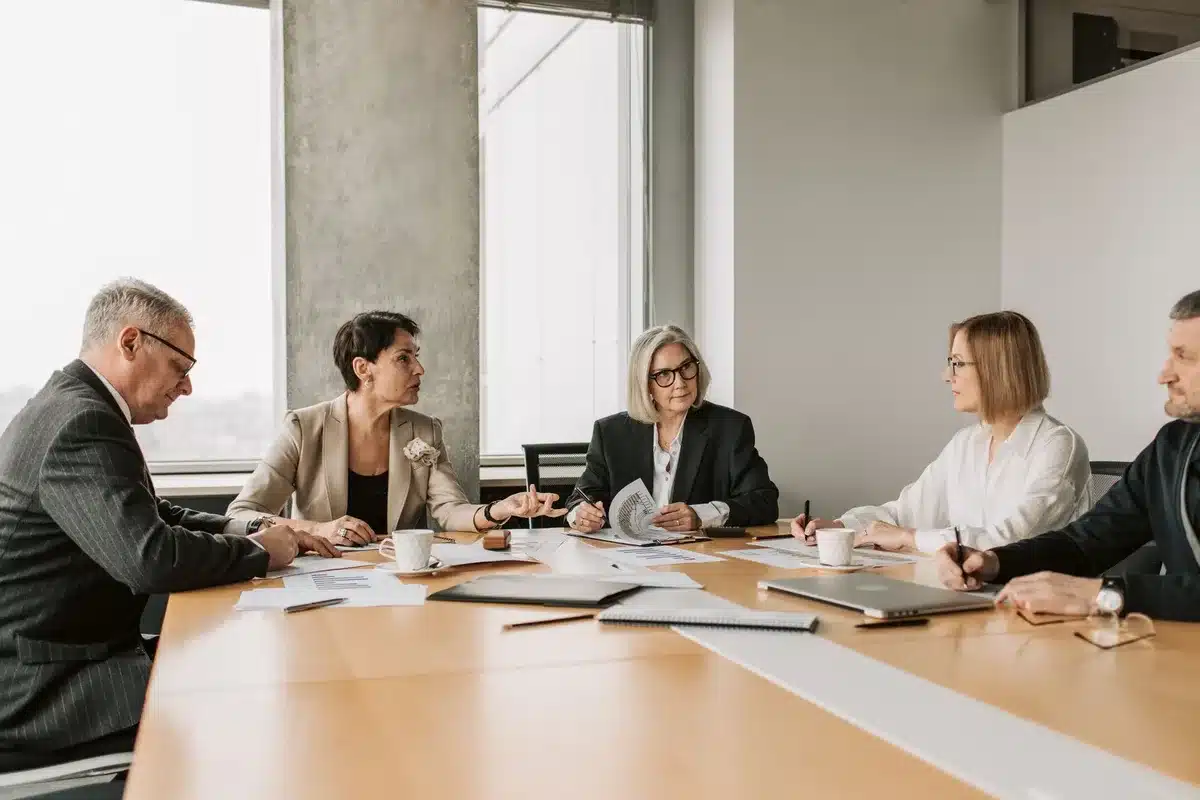 blurred team meeting in modern workspace, anonymous figures around a table with a large screen showing charts