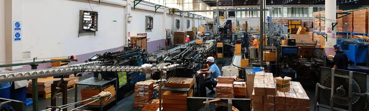 Linha de produção industrial de eletrodomésticos em fábrica, com trabalhadores a montar aparelhos.