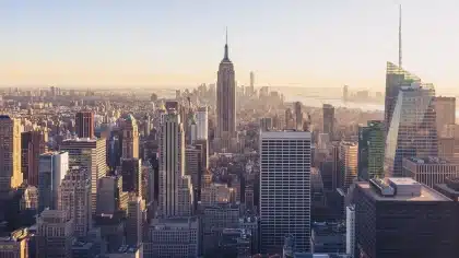 Mesa de redação com dois portáteis e microfone, vista de skyline urbano ao fundo