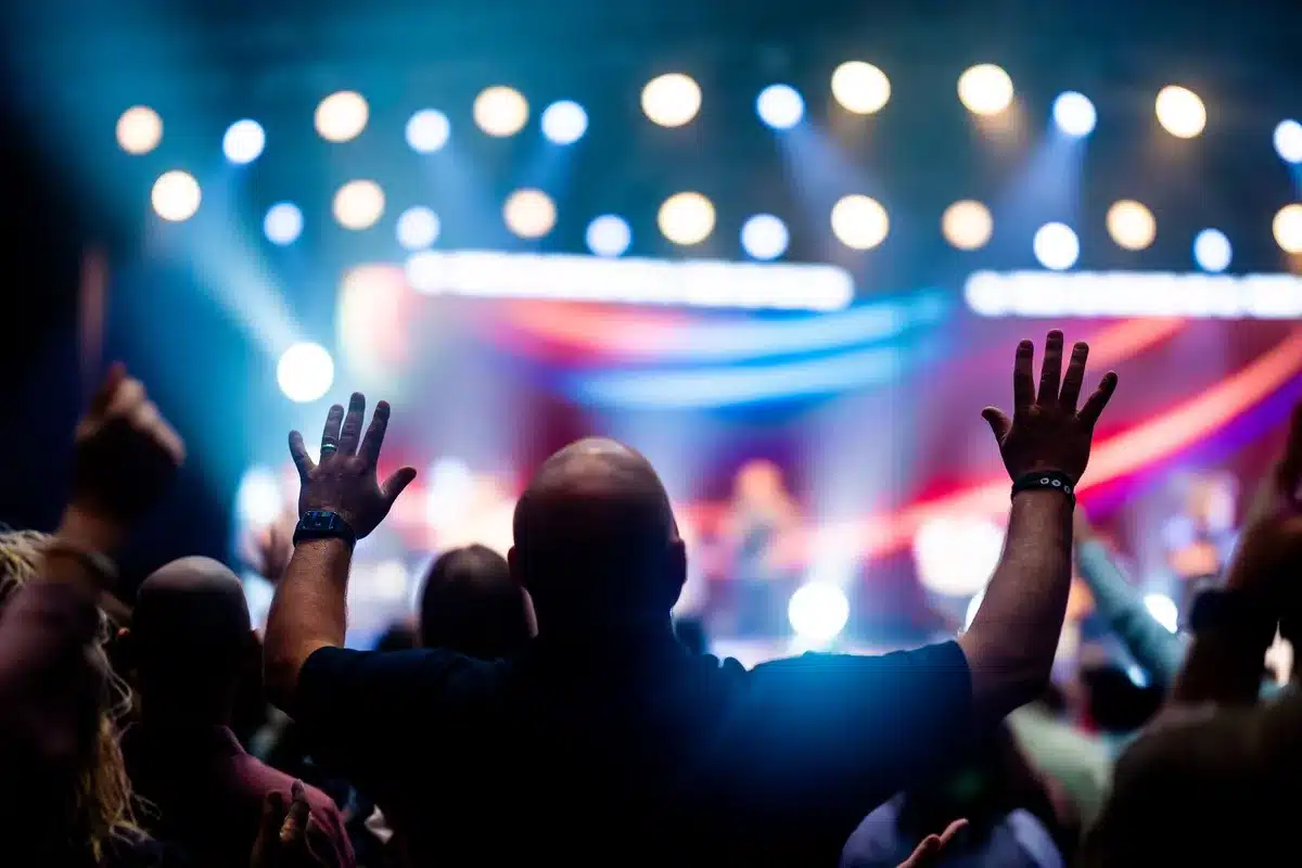 anonymous concert crowd under soft purple lights, silhouettes with raised hands, blurred faces