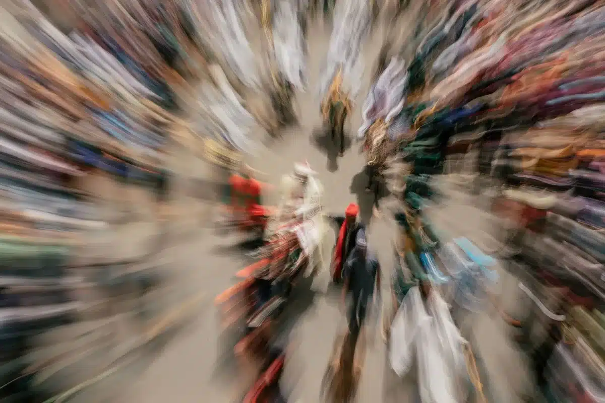 Anonymous crowd of silhouetted people in a dim urban plaza looking up at a large blank billboard, faces turned away and indistinct