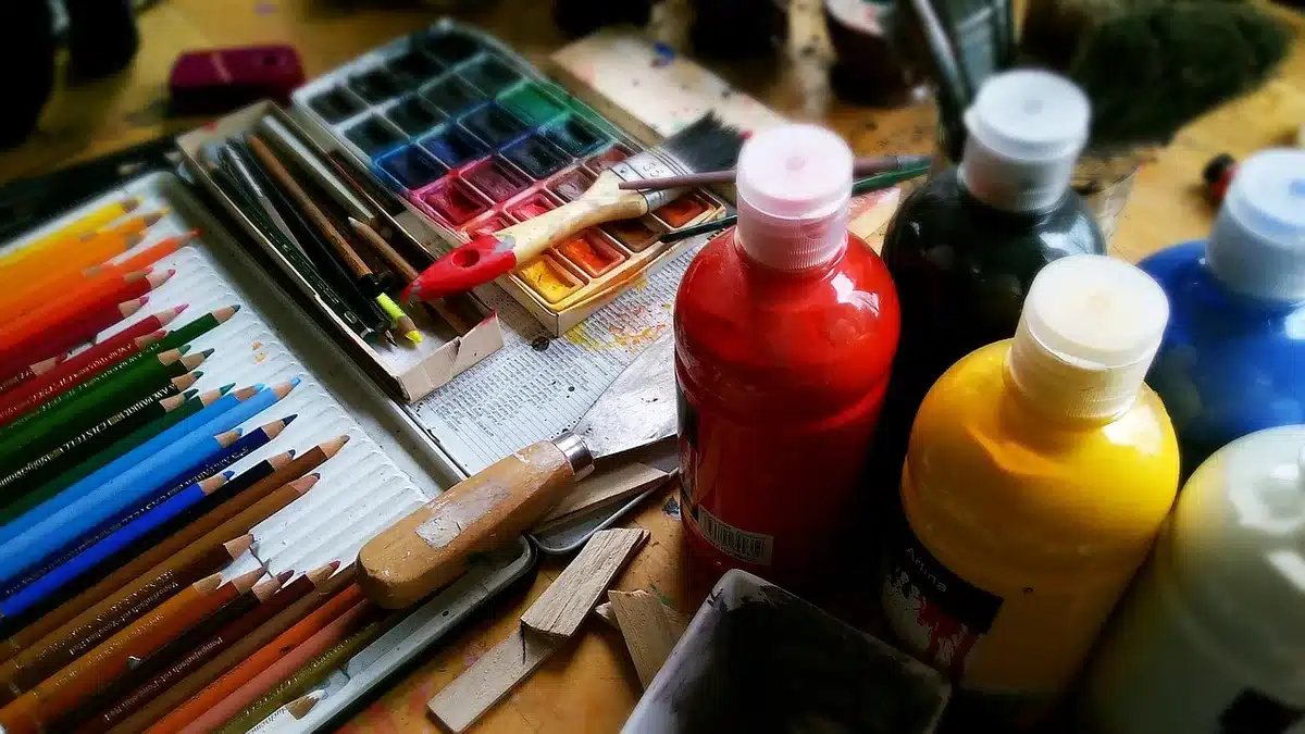 Ateliê com telas texturizadas, tubos de tinta acrílica e mãos a preparar pincéis