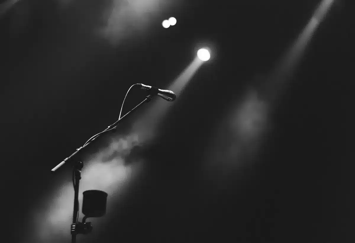 single symbolic microphone on an empty studio stand under a hard spotlight, room behind it dim, dust visible in the beam