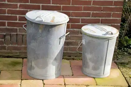 Mãos anónimas seguram garrafas e latas vazias sobre um contentor de reciclagem urbano