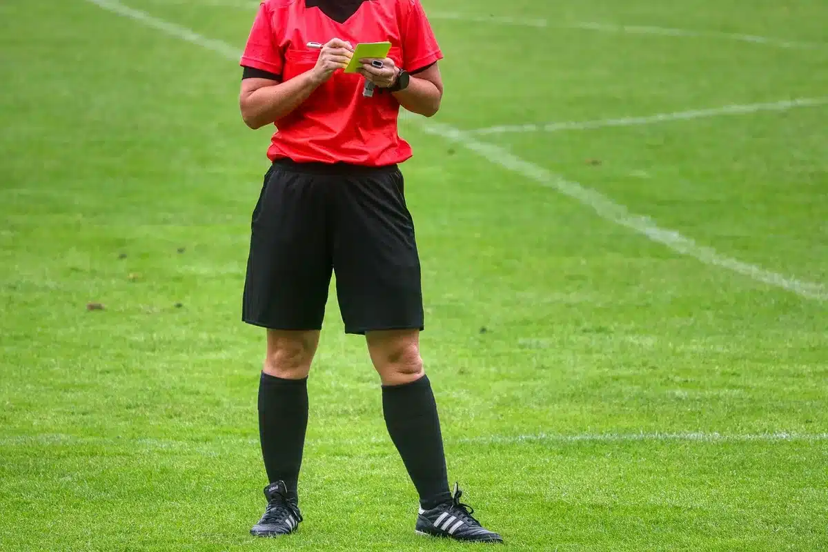 Close-up of an unbranded referee notebook and whistle on a table beside a generic match schedule sheet, no logos visible