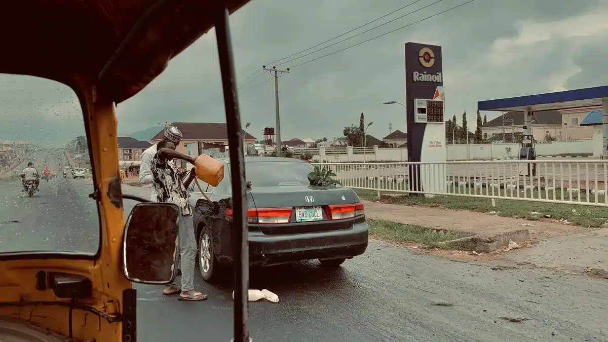 A deserted service station forecourt at dusk, empty pumps and a single fuel price sign blurred in the background