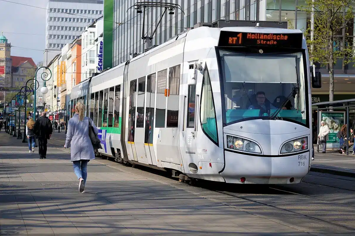 Empty private car parked beside a tram stop at midday, the tram arriving with anonymous passengers visible through windows
