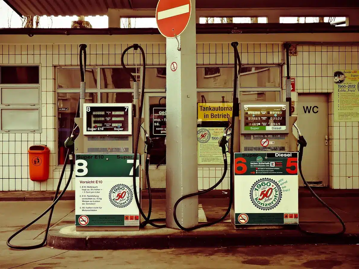 Empty service-station forecourt at dawn, single unattended fuel pump under a canopy, wet tarmac reflecting lights, no brands or signage