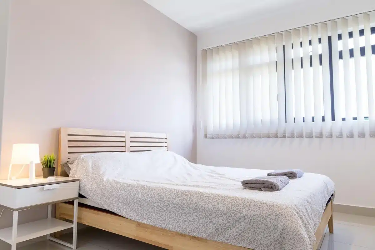 Close-up of a neutral bedroom corner showing an unbranded pillow and folded sheets on a chair, soft natural light from a window, no logos or text visible