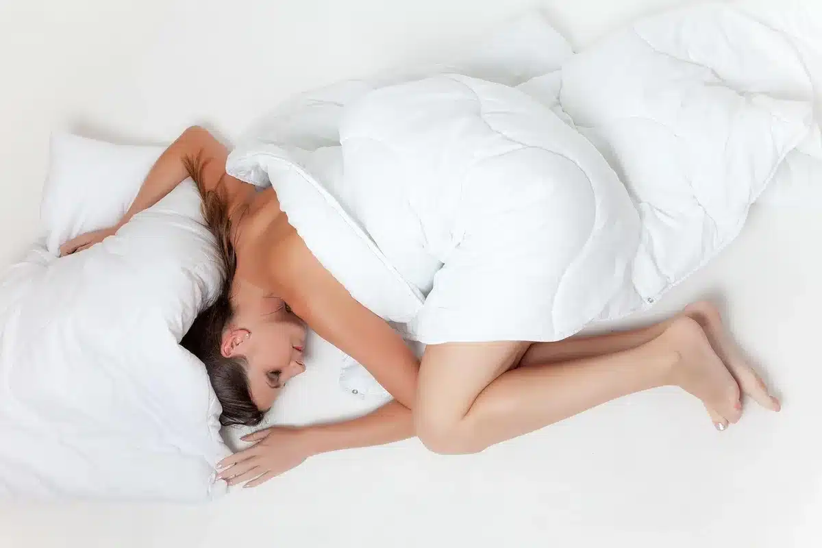 An empty bedroom scene with a neatly made bed covered in a folded, unbranded thermal sheet set on top; soft morning light through a curtained window, a small side table with a lamp — evokes affordable home bedding.