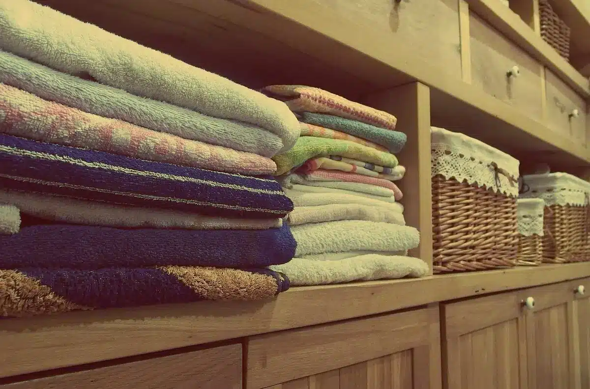 an empty bathroom shelf with neatly folded neutral-colour towels stacked, one towel partially unfurled to show texture