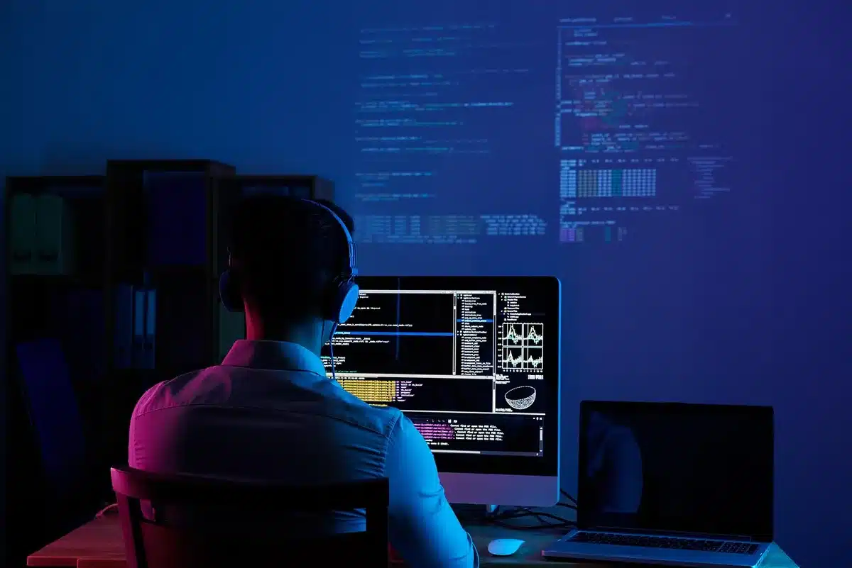 A split workbench with anonymous hands over a laptop screen showing code and a blank notepad, implying model testing and evaluation