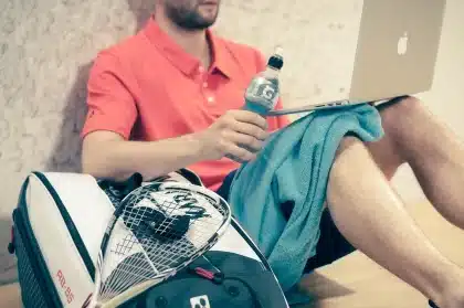Bancada vazia de ténis com raquete e bola em primeiro plano, público em silhueta ao fundo