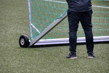 Bota e colete de treino sobre relvado vazio com balizas ao fundo