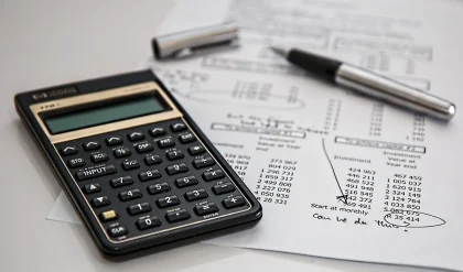 Mãos anónimas com um extrato de crédito e uma calculadora sobre uma mesa de cozinha