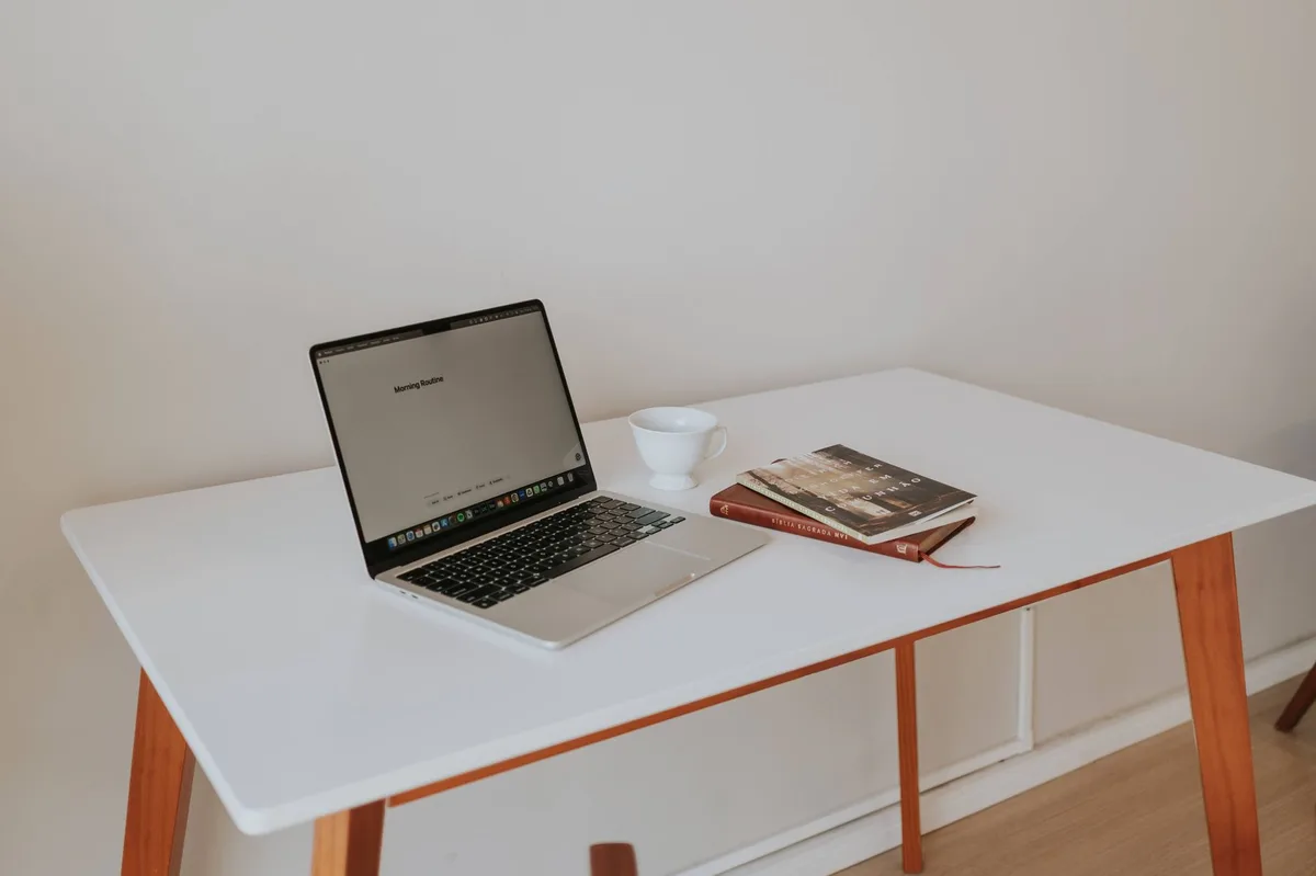 Empty modern office desk with a closed laptop, an unbranded notebook and a pen, a faint glow from a nearby screen suggesting digital work