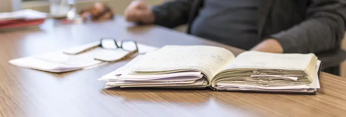 Anonymous hands holding a smartphone with a blank appointment confirmation screen, a paper checklist and a pen on a wooden desk