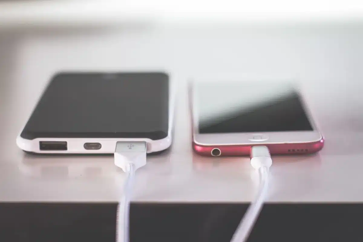close-up of a modern unbranded smartphone on a wooden desk showing a battery icon on screen, soft daylight, no logos