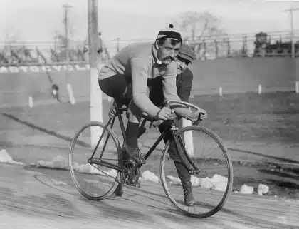 Silhueta de ciclista apoiado no guidão junto à pista de velódromo
