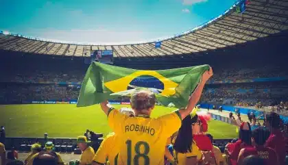 Mãos de adeptos com cachecóis e bilhetes junto à entrada de um estádio vazio