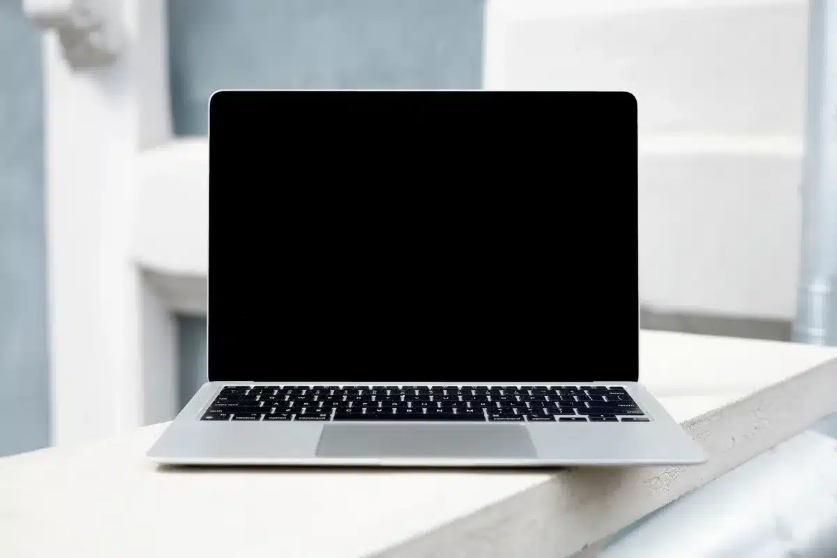 Anonymous silhouette of a person looking at a glowing laptop screen on a desk in a small home office; papers and a coffee cup nearby