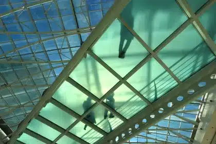 Consumidores anónimos a fazer compras num centro comercial com ecrã de cotações ao fundo