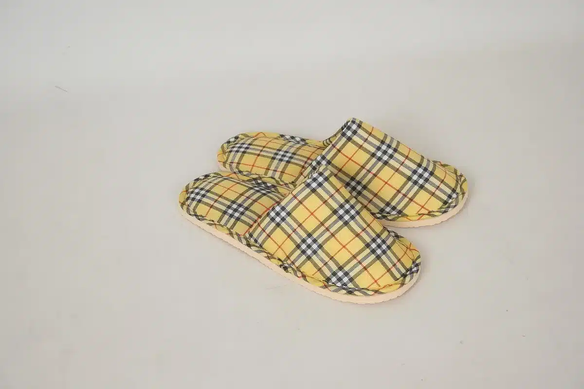 A pair of unbranded fuzzy slide slippers on a wooden shelf, neutral tones and no logos, cozy indoor retail display