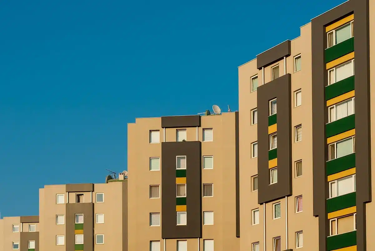 Row of anonymous apartment blocks seen from street level, some windows shuttered, others with balconies empty, late afternoon light