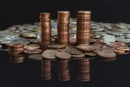 Mãos anónimas sobre um talão bancário, calculadora e moedas mostrando cálculos de rendimentos