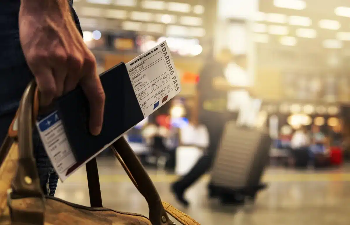 two anonymous travellers checking phone at terminal, boarding passes visible as generic slips, bags at feet