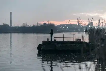 Silhueta de grupo anónimo junto a um porto com bandeiras genéricas e navios ao fundo